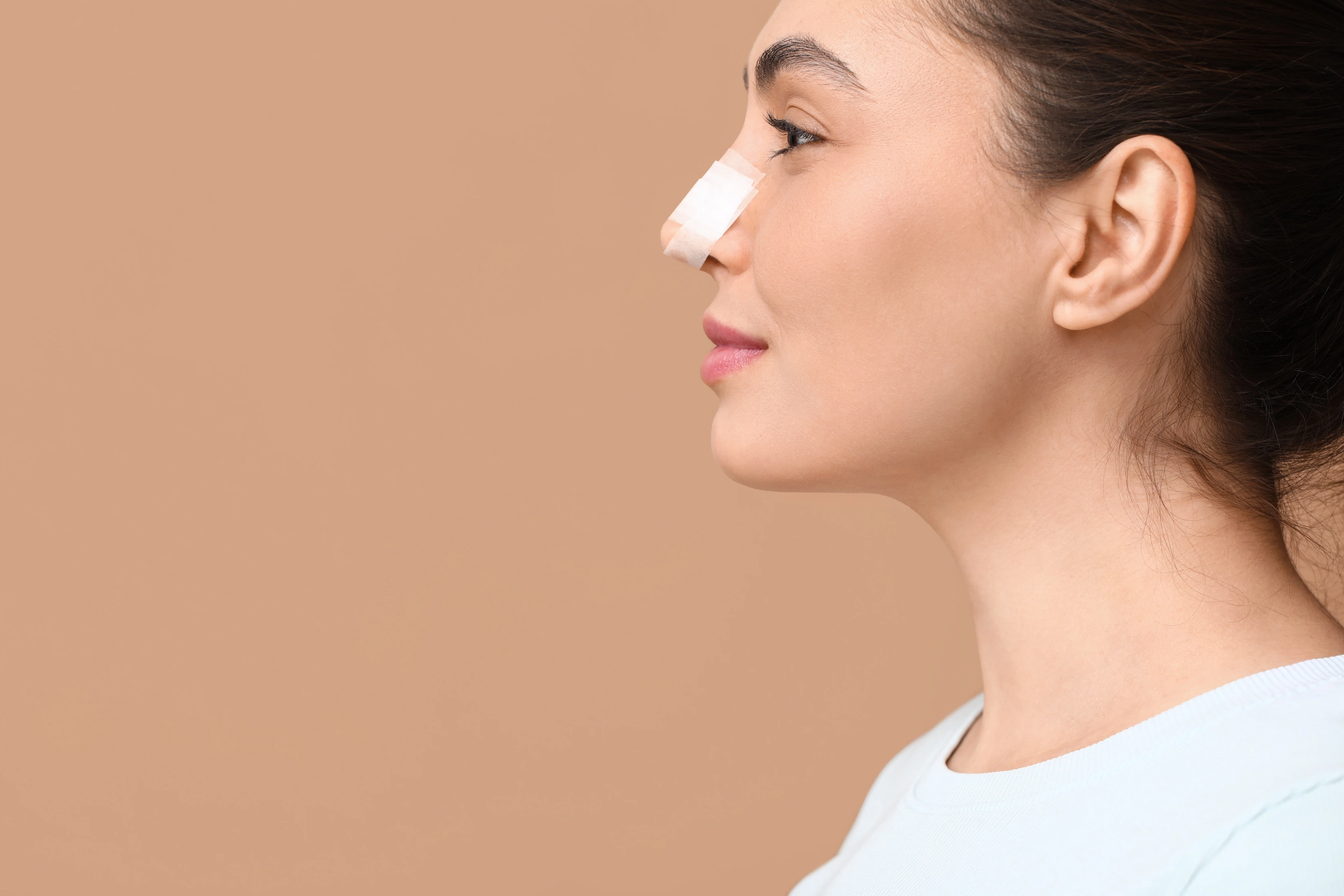 Young woman with bandaged nose on brown background, closeup. Plastic surgery concept